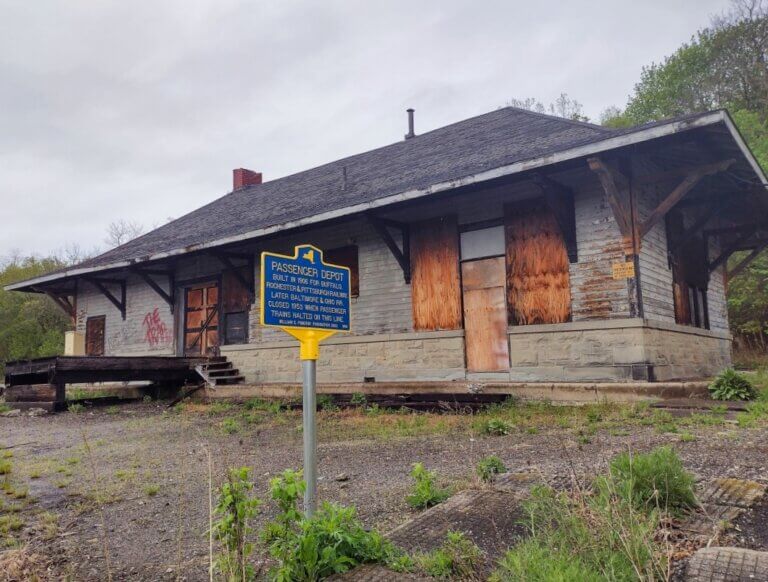 New York State historical marker for passenger depot with original structure in the background. Marker funded by the William G. Pomeroy Foundation.